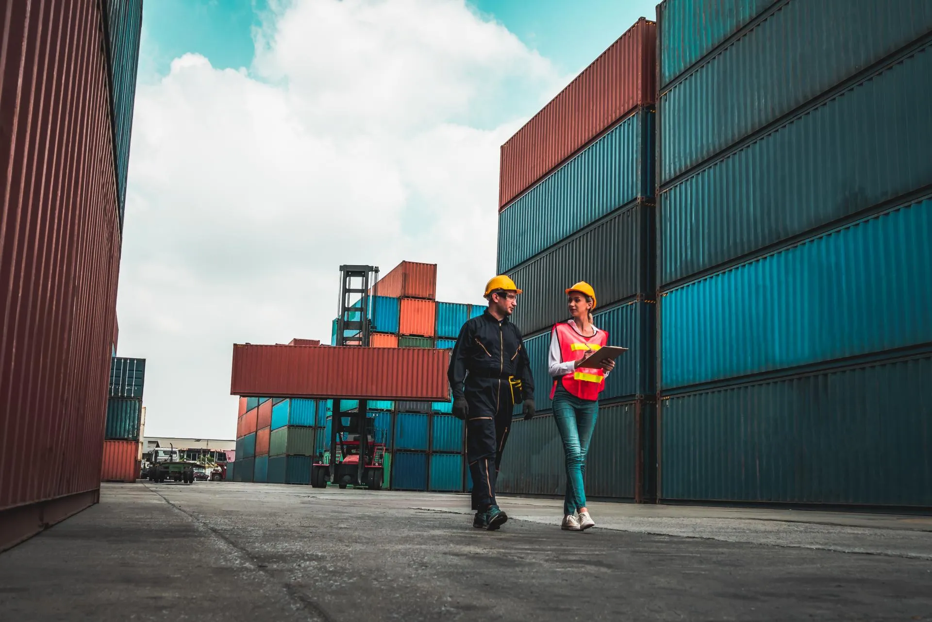 in safety helmets walking between stacked shipping containers