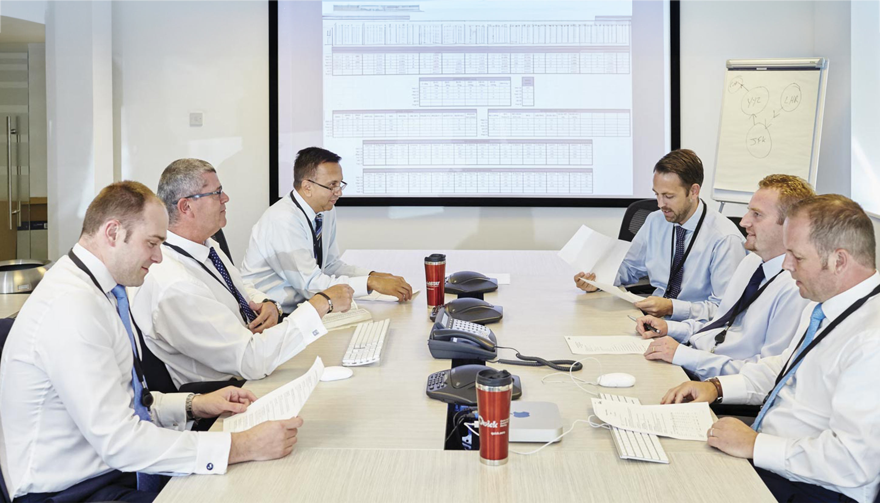 6 colleagues around a table in a conference room, having a meeting