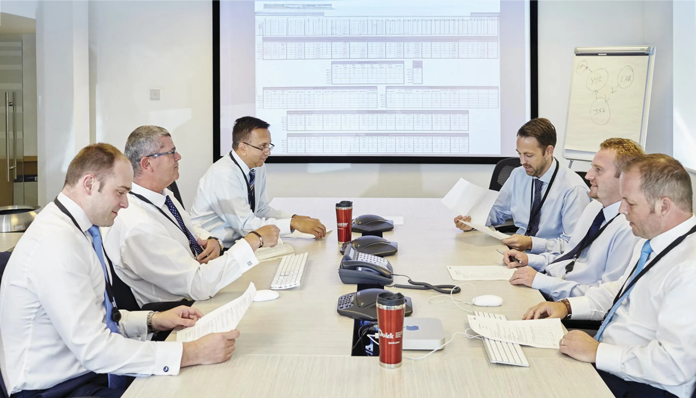 6 colleagues around a table in a conference room, having a meeting