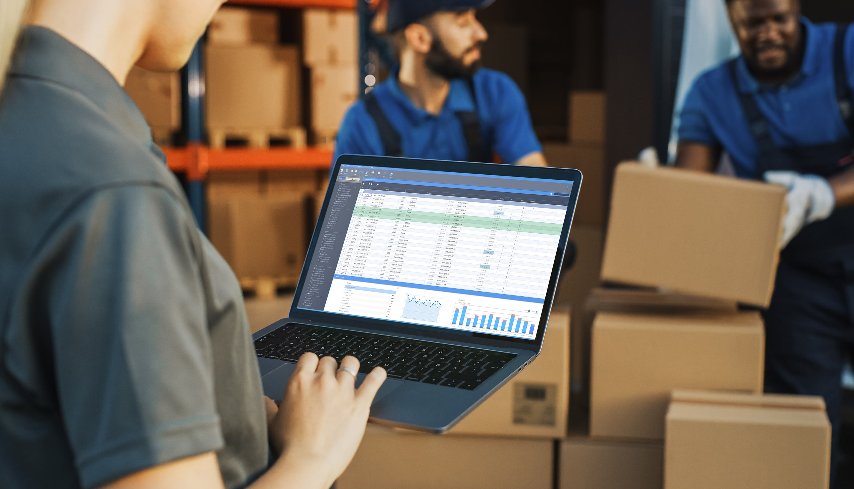 Female worker typing on laptop, 2 male workers moving boxes in the background