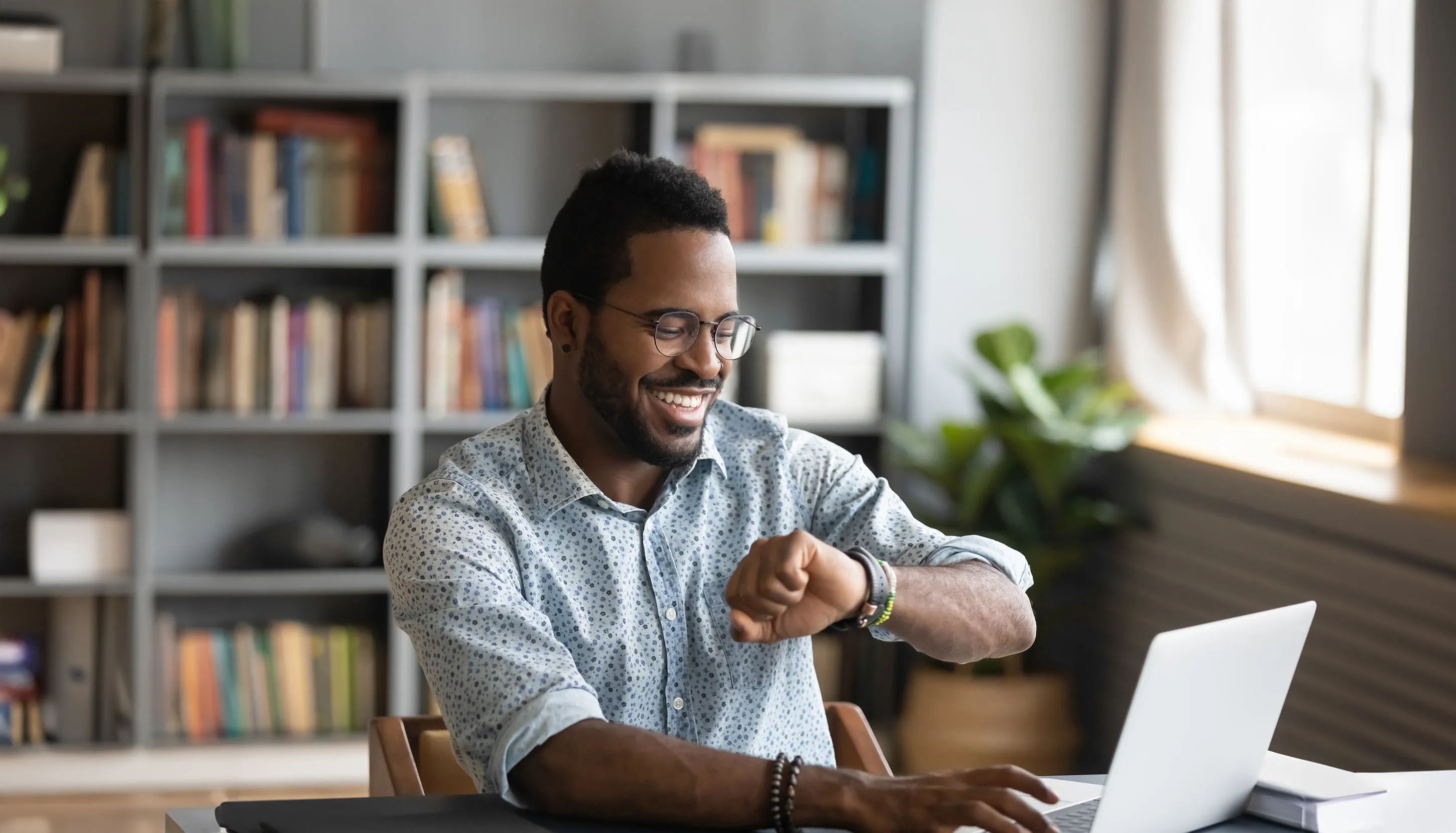 Man looking at his watch, typing on laptop