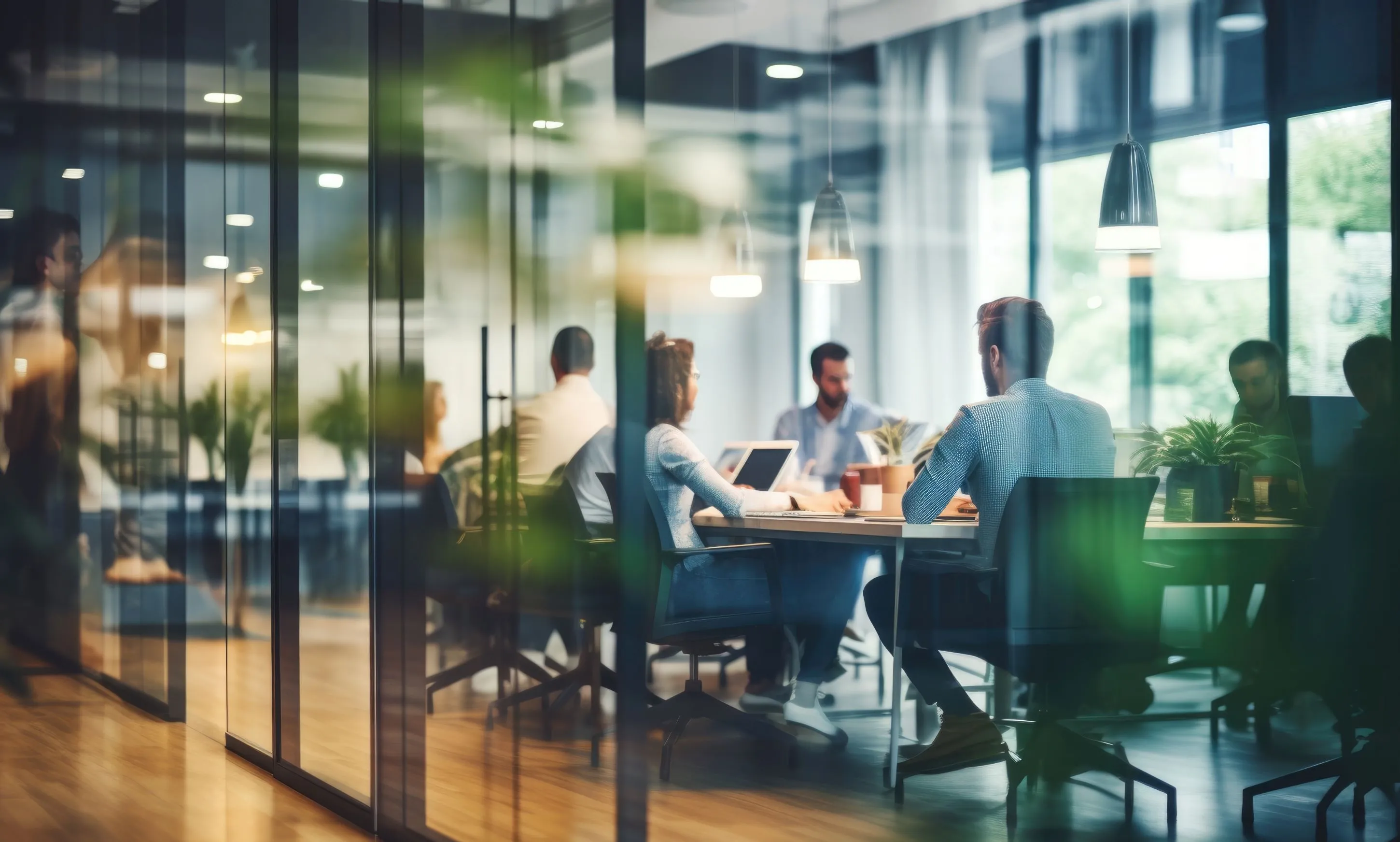 Team of colleagues sitting at a meeting table seen through glass walls